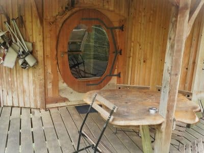 Cabane en bois avec une porte ronde et une table en bois sur la terrasse.