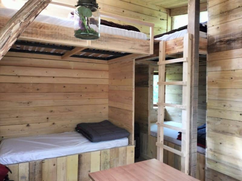 Cabane en bois avec lits superposés et lumière suspendue, ambiance chaleureuse.