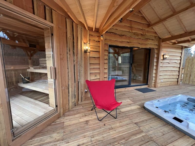 Chalet en bois avec sauna, jacuzzi et coin détente sur une terrasse en bois.