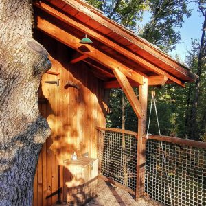 Cabane perchée en bois, entourée darbres, avec une terrasse suspendue.