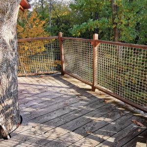 Cabane perchée dans un arbre avec une terrasse en bois entourée de verdure.