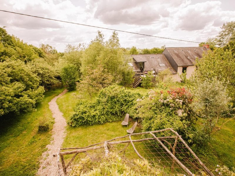 Gîte charmant entouré de verdure, avec un chemin sinueux et des chaises relaxantes.