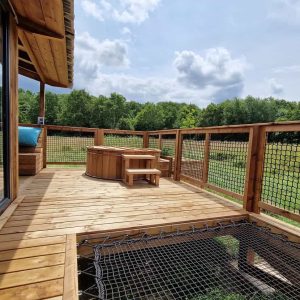 Cabane en bois avec terrasse et jacuzzi, vue sur la nature verdoyante.