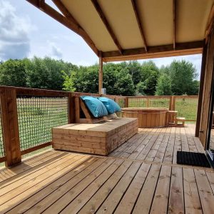 Cabane en bois avec terrasse ensoleillée et coussins confortables, vue sur la nature.