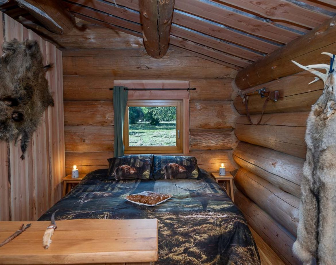 Cabane en bois avec lit douillet, décorée déléments naturels et vue sur la nature.