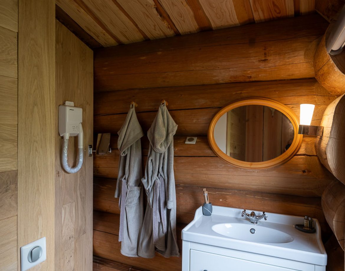 Hébergement insolite en bois à Champagne-Ardenne, avec salle de bain moderne et miroir rond.