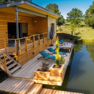Cabane en bois sur pilotis avec terrasse et vue sur un étang paisible.
