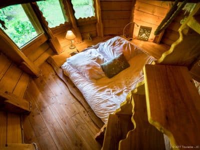 Chalet en bois avec lit douillet et lumière douce, entouré de nature verdoyante.