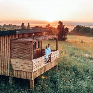 Cabane en bois sur pilotis, avec vue sur un coucher de soleil dans les champs.