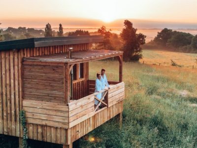 Cabane en bois sur pilotis, avec vue sur un coucher de soleil dans les champs.