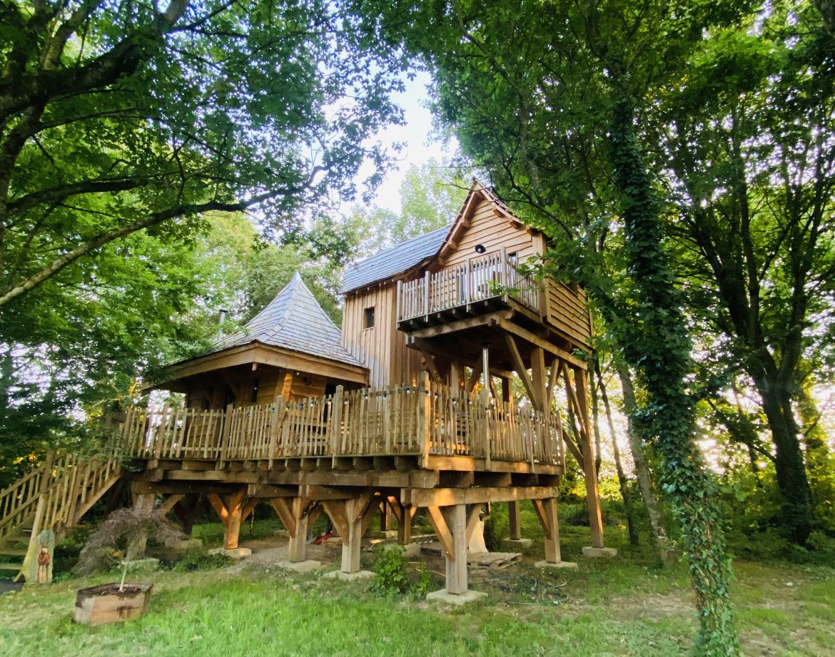 Cabane perchée en bois, entourée darbres verdoyants en Bretagne.