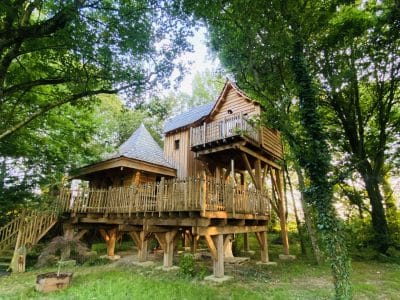 Cabane perchée en bois, entourée darbres verdoyants en Bretagne.