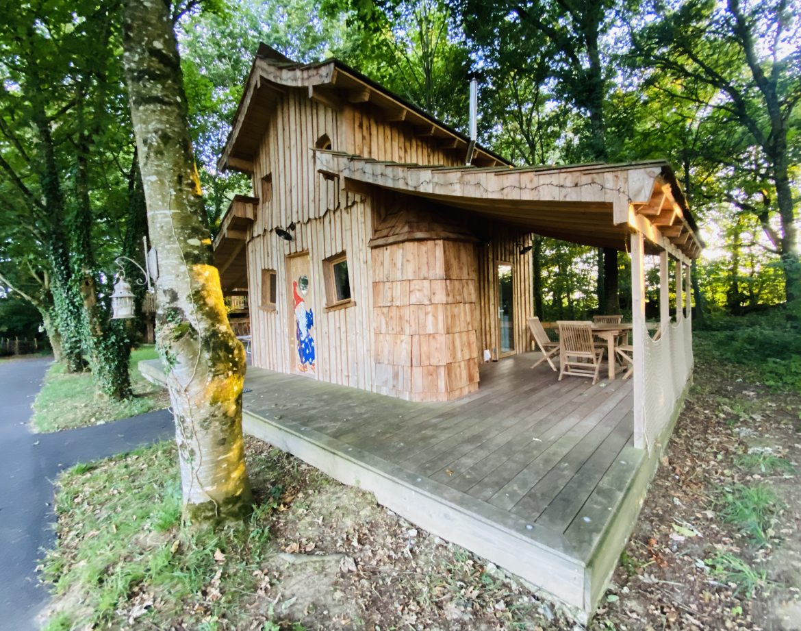 Cabane en bois en Bretagne, entourée darbres, avec terrasse en bois accueillante.