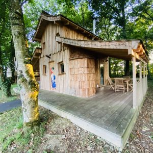 Cabane en bois en Bretagne, entourée darbres, avec terrasse en bois accueillante.
