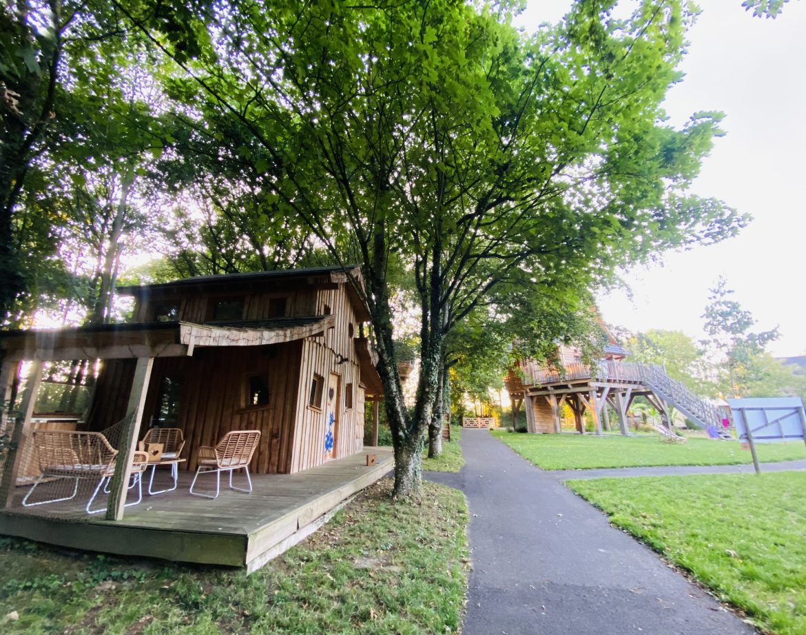Cabane en bois en Bretagne, entourée darbres, avec terrasse et mobilier extérieur.