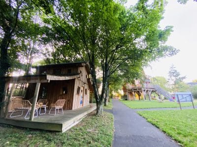 Cabane en bois en Bretagne, entourée darbres, avec terrasse et mobilier extérieur.