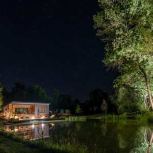 Cabane en bois au bord dun étang, illuminée sous un ciel étoilé en Aquitaine.