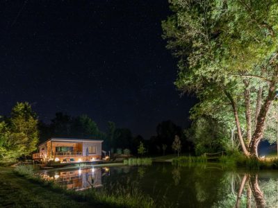 Cabane en bois au bord dun étang, illuminée sous un ciel étoilé en Aquitaine.