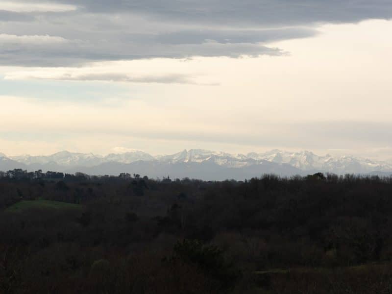 Vue panoramique depuis un gîte rural, avec les montagnes enneigées en arrière-plan.