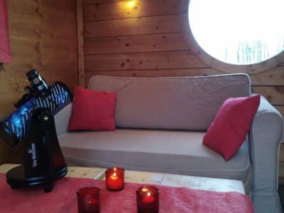Cabane en bois avec un télescope et des bougies, ambiance cosy et chaleureuse.