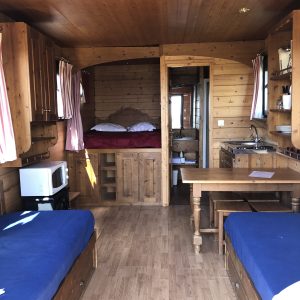 Cabane en bois cosy avec lits jumeaux et coin cuisine, ambiance chaleureuse.