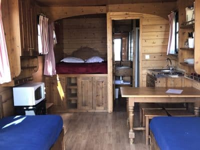 Cabane en bois cosy avec lits jumeaux et coin cuisine, ambiance chaleureuse.