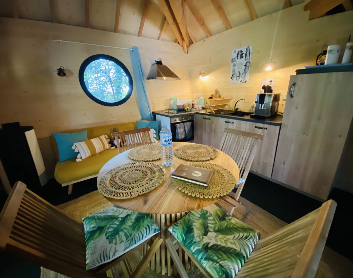 Cabane en bois en Bretagne, avec un coin cuisine et une grande fenêtre ronde.