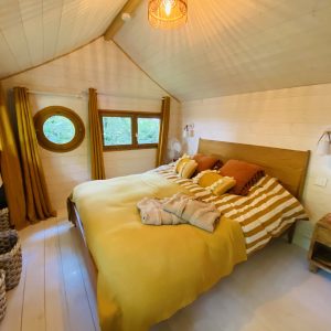 Chalet cosy en Bretagne, avec un lit douillet et des rideaux dorés.