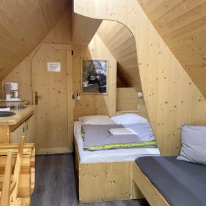 Chalet en bois chaleureux avec lit confortable et coin cuisine, ambiance cocooning.