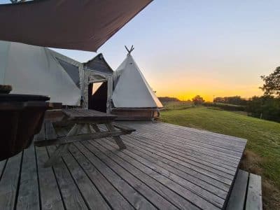 Tipi en Midi-Pyrénées avec terrasse en bois, vue sur un coucher de soleil.