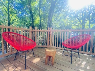 Hébergement insolite en Bretagne : deux chaises rouges sur une terrasse boisée.