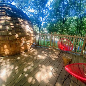 Hébergement insolite en Bretagne : cabane en bois avec terrasse ensoleillée et fauteuils rouges.