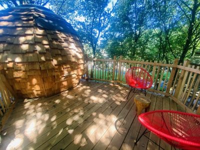 Hébergement insolite en Bretagne : cabane en bois avec terrasse ensoleillée et fauteuils rouges.
