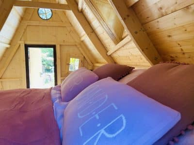 Cabane en bois en Bretagne, lit douillet avec coussins colorés et vue sur la nature.