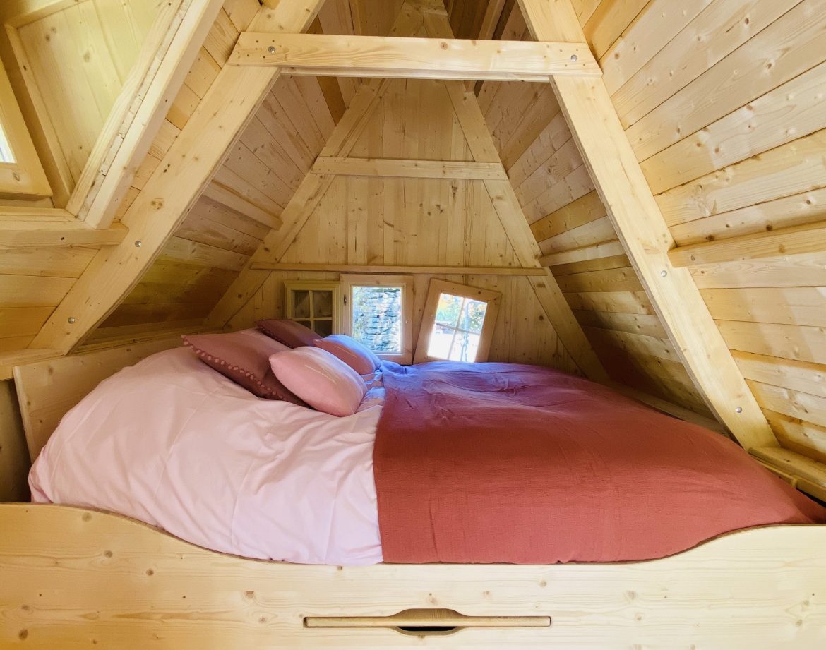 Cabane en bois en Bretagne, lit douillet sous un toit en pente avec fenêtres lumineuses.