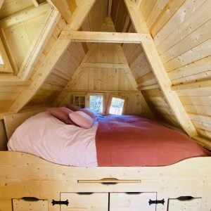 Cabane en bois en Bretagne, lit douillet sous un toit en pente avec fenêtres lumineuses.
