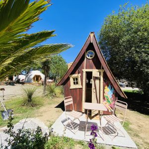 Cabane en bois colorée en Bretagne, avec table et chaises sur la terrasse ensoleillée.