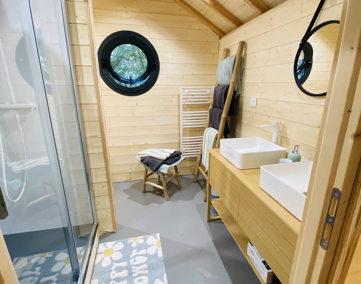 Hébergement insolite en Bretagne : salle de bain en bois avec fenêtre ronde et douche spacieuse.