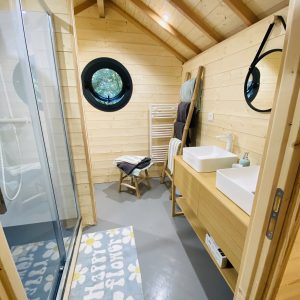 Hébergement insolite en Bretagne : salle de bain en bois avec fenêtre ronde et douche spacieuse.