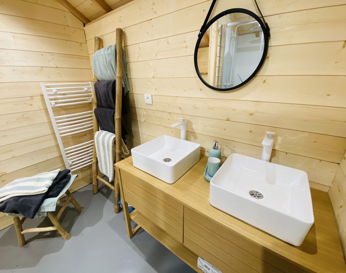 Salle de bain moderne en bois avec double vasque dans un hébergement insolite en Bretagne.