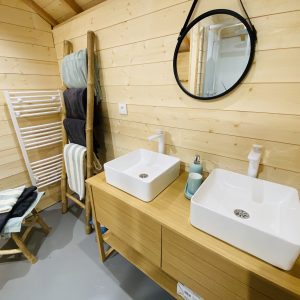 Salle de bain moderne en bois avec double vasque dans un hébergement insolite en Bretagne.