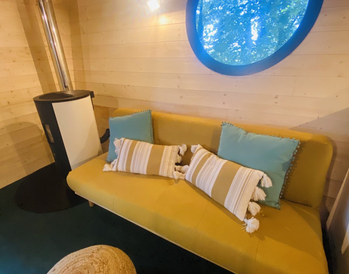 Hébergement insolite en Bretagne : intérieur cosy avec un canapé jaune et fenêtre ronde.