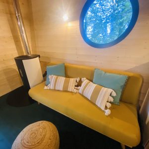 Hébergement insolite en Bretagne : intérieur cosy avec un canapé jaune et fenêtre ronde.