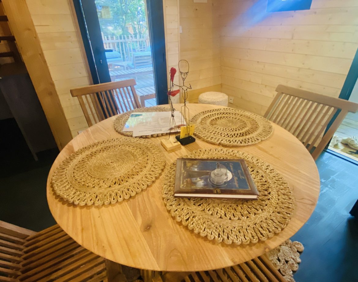Hébergement insolite en Bretagne : chalet en bois avec table ronde et chaises en rotin.