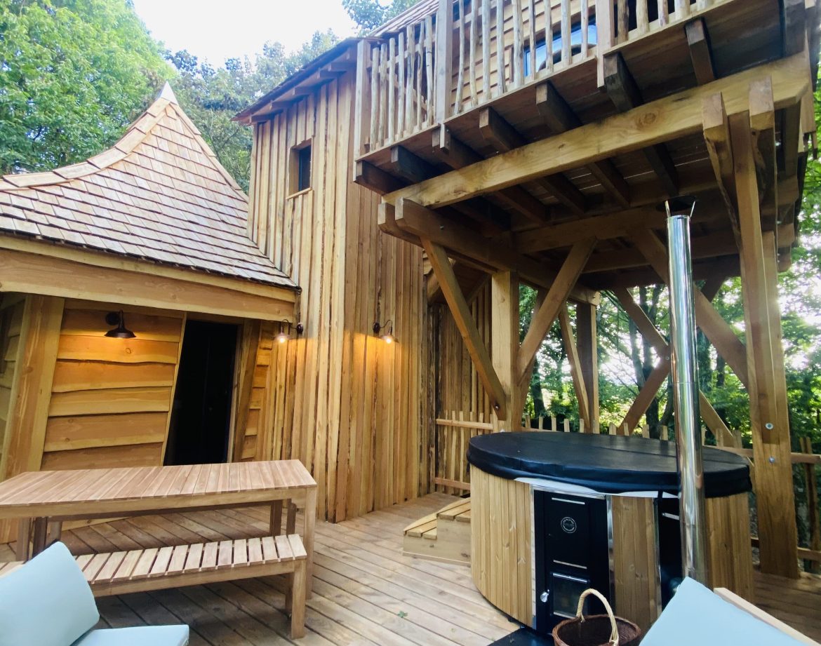 Cabane en bois avec terrasse et jacuzzi, nichée dans la verdure de Bretagne.