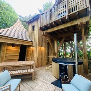 Cabane en bois avec terrasse et jacuzzi, nichée dans la verdure de Bretagne.