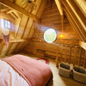 Chalet en bois avec un lit douillet et une fenêtre ronde, ambiance chaleureuse.
