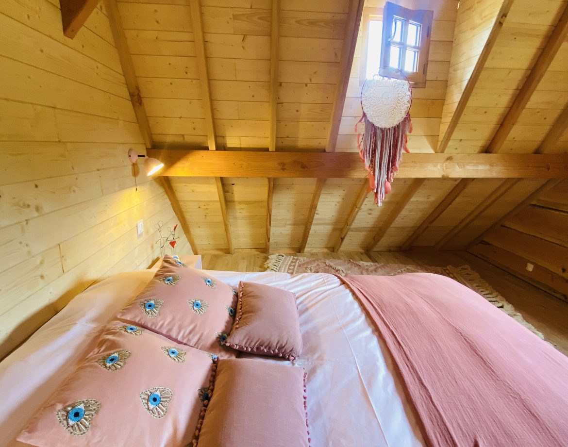 Chalet en bois en Bretagne, avec une literie colorée et un plafond en poutres apparentes.