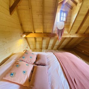 Chalet en bois en Bretagne, avec une literie colorée et un plafond en poutres apparentes.