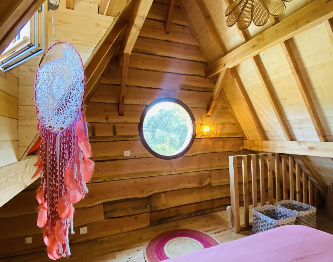 Chalet en bois en Bretagne, avec un plafond en poutres et une fenêtre ronde.